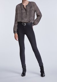 Schwarze Bluse mit Leopardenmuster und Knöpfen, kombiniert mit schwarzen Skinny Jeans und schwarzen Schnürstiefeln, die eine figurbetonte Silhouette präsentieren.