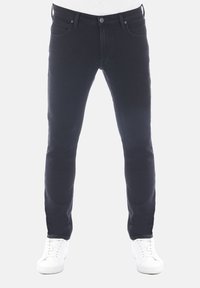 Vaqueros de denim negro con corte slim, diseño de cinco bolsillos, costuras en contraste y cierre de botón, combinados con zapatillas blancas.