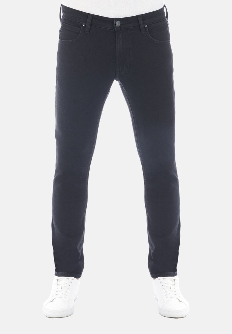 Vaqueros de denim negro con corte slim, diseño de cinco bolsillos, costuras en contraste y cierre de botón, combinados con zapatillas blancas.