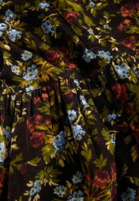 Ciemny materiał z kwiatowym wzorem, w którym widoczne są małe niebieskie, czerwone i żółte kwiaty oraz zielone liście, z detalami ściegów zaciągniętych.