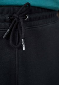 Zwarte sweatpants met een gestructureerde afwerking en een elastische tailleband, voorzien van een zwarte trekkoord met een metalen aglet, afgewerkt met een klein logo.