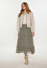 Lys beige læder bomberjakke med en brun pelskrave, parret med en lagdelt sort blomsterkjole og beige snørebåndsstøvler.