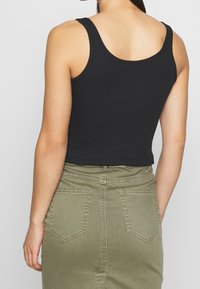 Top corto negro de algodón con una textura suave, combinado con una falda verde de cintura alta que presenta bolsillos traseros y detalles de costura.