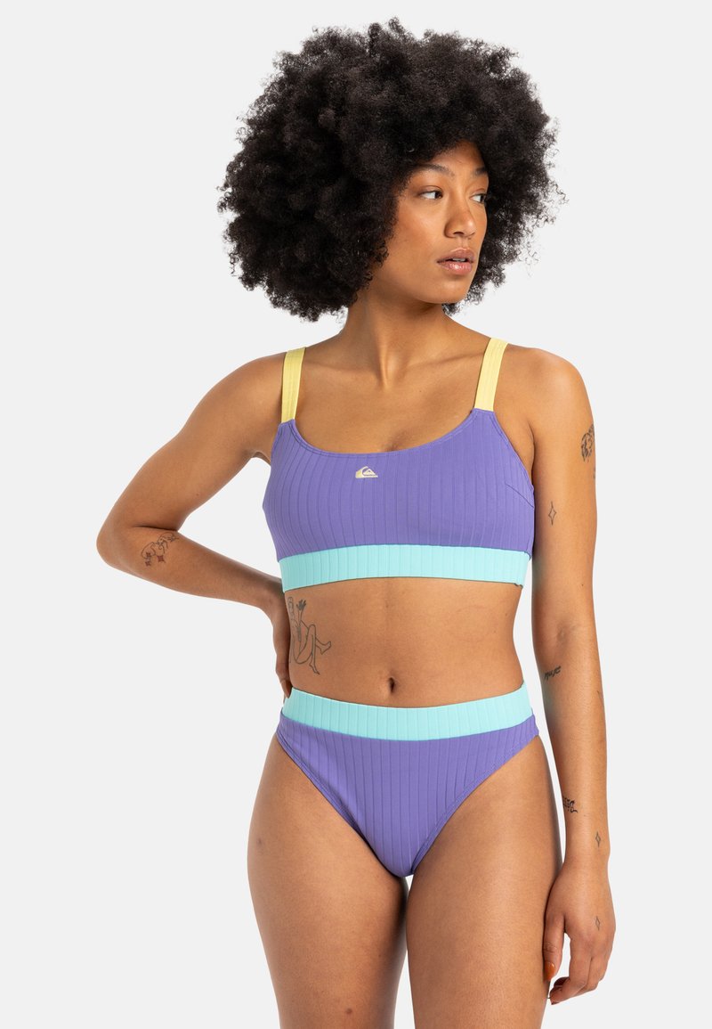 Two-piece swimwear set with ribbed texture. Top is purple with yellow straps; bottom is purple with a turquoise band.