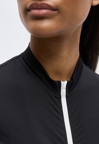 Κοντινό πλάνο στο κάτω μέρος του προσώπου και τον λαιμό ενός ατόμου που φοράει μαύρο επάνω με φερμουάρ σε λευκό χρώμα, κλεισμένο μέχρι το γιακά.