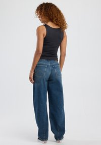 Black fitted tank top paired with loose-fit blue denim jeans, featuring back pockets and subtle stitching details.