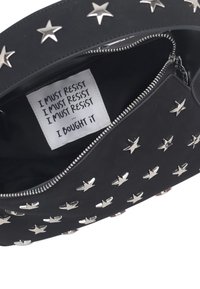 Borsa in pelle nera con borchie a forma di stella in argento. L'interno presenta un'etichetta con la scritta "DEVO RESISTERE" e "L'HO COMPRATA". Chiusura con cerniera visibile.