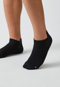 Schwarze Knöchelsocken aus einem strukturierten Material, mit einem niedrigen Schnitt, der gerade über dem Knöchel sitzt, und einem kleinen weißen Logo auf einer Seite.