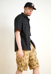 Black short-sleeve shirt with two chest pockets, paired with beige camo cargo shorts featuring side pockets and a textured pattern.