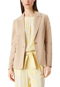 Beige blazer met een getailleerde pasvorm, met schoudernaden, enkele knoopsluiting en zijzakken, gecombineerd met een lichtgele bedrukte top.