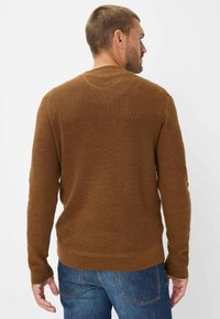 Bruine sweater met een ribbeltextuur, ronde halslijn en lange mouwen, gecombineerd met blauwe denim jeans. De achterkant toont een strak ontwerp.