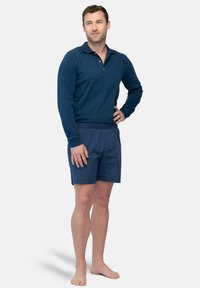 Navy lange mouwen polo shirt met knopen, gecombineerd met blauw geruite shorts. De stof lijkt lichtgewicht met een elastische tailleband.