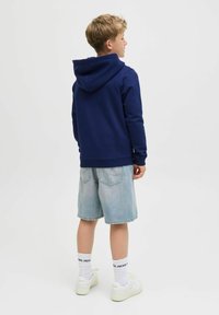 Marinblå hoodie med dragsko, i kombination med ljusblå jeansshorts. Vita sneakers och vita strumpor med svart logodetalj.