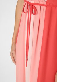 Czerwona i różowa plisowana sukienka z dopasowanym sznurkiem w talii. Materiał jest lekki i gładki, z dwoma sekcjami w blokach kolorystycznych.