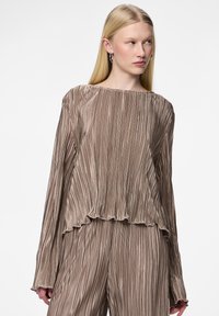 Haut long à manches texturé et plissé en taupe métallique avec un ourlet à volants et un col large, présenté sur un fond neutre.