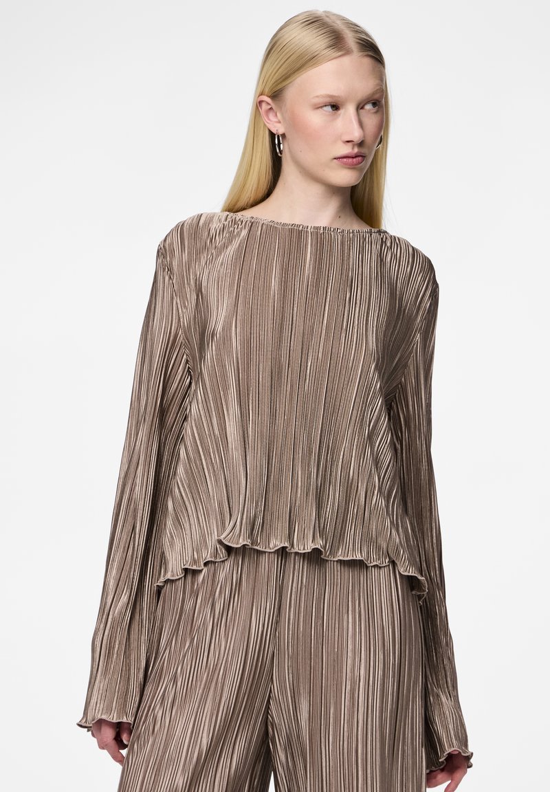 Haut long à manches texturé et plissé en taupe métallique avec un ourlet à volants et un col large, présenté sur un fond neutre.