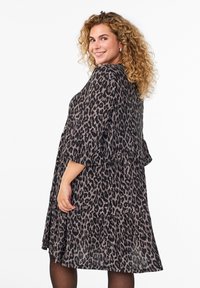 Robe à imprimé léopard avec des manches trois-quarts, un design en couches et une texture douce. Les couleurs incluent le noir et des tons beige atténués.