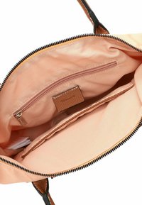 Interno della borsa a tracolla in tessuto pesca, presenta una tasca con zip e uno spazio per carte con un accento testurizzato marrone. Rifiniture in zip nera e manico.