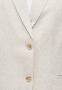 Beezh linane bleiser sälgutatud kraega, millel on kaks ümmargust helepruuni nööpi ja küljetasku. Tekstuuriga kangas peene soonikuga.