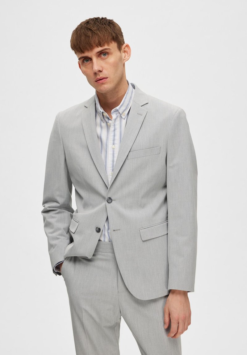 Chaqueta de traje gris claro hecha de una tela suave con solapa de muesca, cierre de un solo botón y una textura sutil, combinada con una camisa a rayas.