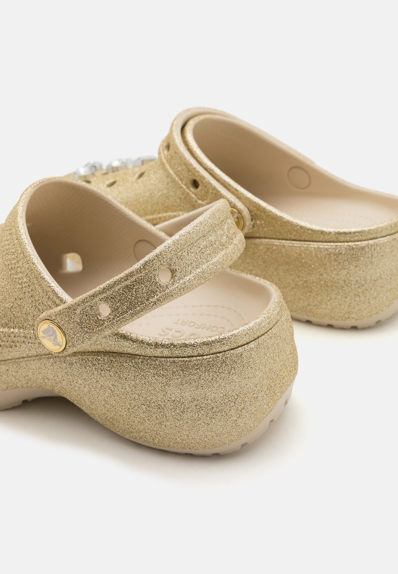 Zuecos de purpurina dorada con una correa ajustable, fabricados en un material ligero, con un upper texturizado y una plantilla suave y contorneada.