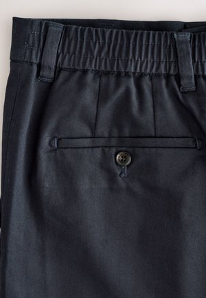 Nahaufnahme des Bundes einer dunkelblauen Hose mit elastischem Rückenteil, Gürtelschlaufen und einer einzelnen mit Knopf verschlossenen hinteren Leistentasche.