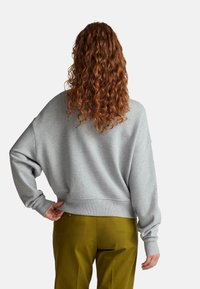 Felpa grigia con spalle scese, polsini e orlo a coste; abbinata a pantaloni verdi. Presenta una vestibilità comoda e una texture morbida.