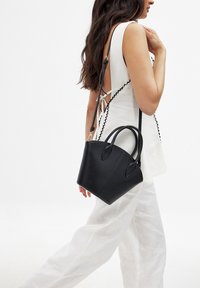 Bolso de mano de cuero negro con asas dobles y una correa de hombro desmontable, que presenta un diseño estructurado y una textura suave.