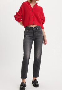 Jersey corto rojo acanalado con escote en V y cierre de botones, combinado con jeans negros de cintura alta y mocasines negros.