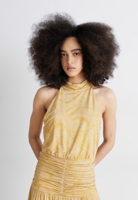 Žuti halter top s mramornim uzorkom od teksturirane tkanine, s nabranim pojasom i bez rukava. Glatka drapiranja kroz cijeli komad.