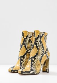 Bottes basses à imprimé serpent jaune et noir avec un bout carré et une finition texturée, dotées d'un talon épais et d'une fermeture éclair latérale.