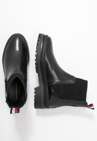 Mustat nilkkurit, joissa on teksturoitu nahkapinta, joustavat sivut ja paksu kumipohja. Varressa on kolmivärinen vetonauha.