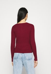 Vínová žebrovaná svetr s dlouhými rukávy, kulatým výstřihem a úzkým lemem. V kombinaci se světle modrými džíny s vysokým pasem.