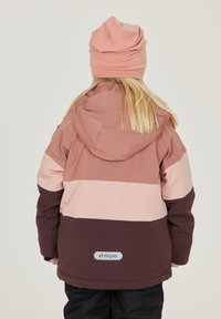 Rosa och mauve färgblockerad jacka med huva, med en brun nedre del och en "ZIGZAG" logotyp på baksidan, bärs med en matchande mössa.