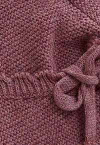 Nahaufnahme eines strukturierten, staubrosa Strickstoffs mit geripptem Rand und gebundenem Kordeldetail.