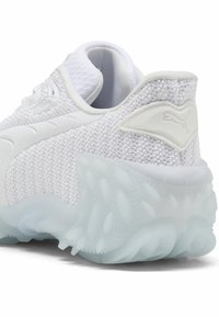 Valkoinen verkkomallinen urheilukenkä, jossa on kuvioitu päällinen, pehmustettu kaulus ja läpikuultava, paksu pohja. Koristaa hienovarainen logoyksityiskohta kantapäällä.