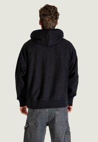 Sudadera negra con capucha y corte holgado. Presenta puños y dobladillo acanalados, textura suave y detalles de costura. Combina con pantalones cargo grises.