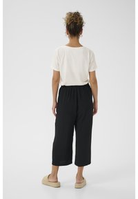 Biela krátka rukávová tričko, voľné čierne culottes a béžové slip-on topánky. Oblečenie je s voľným strihom a textúrovanou tkaninou.