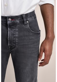 Jeans in denim grigio scuro con una vestibilità slim, caratterizzati da cinque tasche, una chiusura a bottone e cuciture rosse sottili sulla cintura.