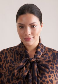 Blusa con stampa leopardata in marrone e blu navy con un grande fiocco al collo. Tessuto morbido, vestibilità rilassata e maniche lunghe. Motivo animale dettagliato su tutta la superficie.
