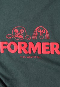 Dark green fabric featuring bold red text that says "FORMER" and playful red drawings of two faces expressing different emotions.