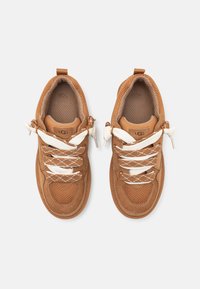 Baskets brunes avec un mélange de matériaux en daim et en maille, dotées de lacets blancs, de cols rembourrés et d'accents texturés sur les côtés.