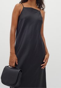 Czarna satynowa sukienka na ramiączkach o luźnym fasonie, w połączeniu z usztywnioną czarną torebką na rękę.