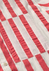 Röd och vit randig skjorta med knapppDetail, med en texturerad tyg och en ficka. Horisontella ränder varierar i bredd.