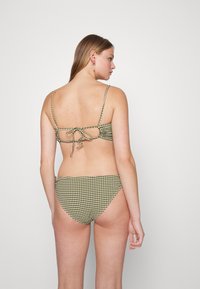 Conjunto de bikini verde e branco com padrão xadrez, com alças finas e amarração nas costas. A parte de baixo apresenta um corte baixo que combina com o design da parte de cima.
