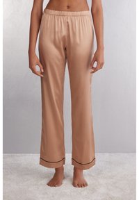 Satin pyjamabroek in lichtbeige met een elastische tailleband, rechte pijpen en zwarte bies langs de zoom. Soepele textuur.