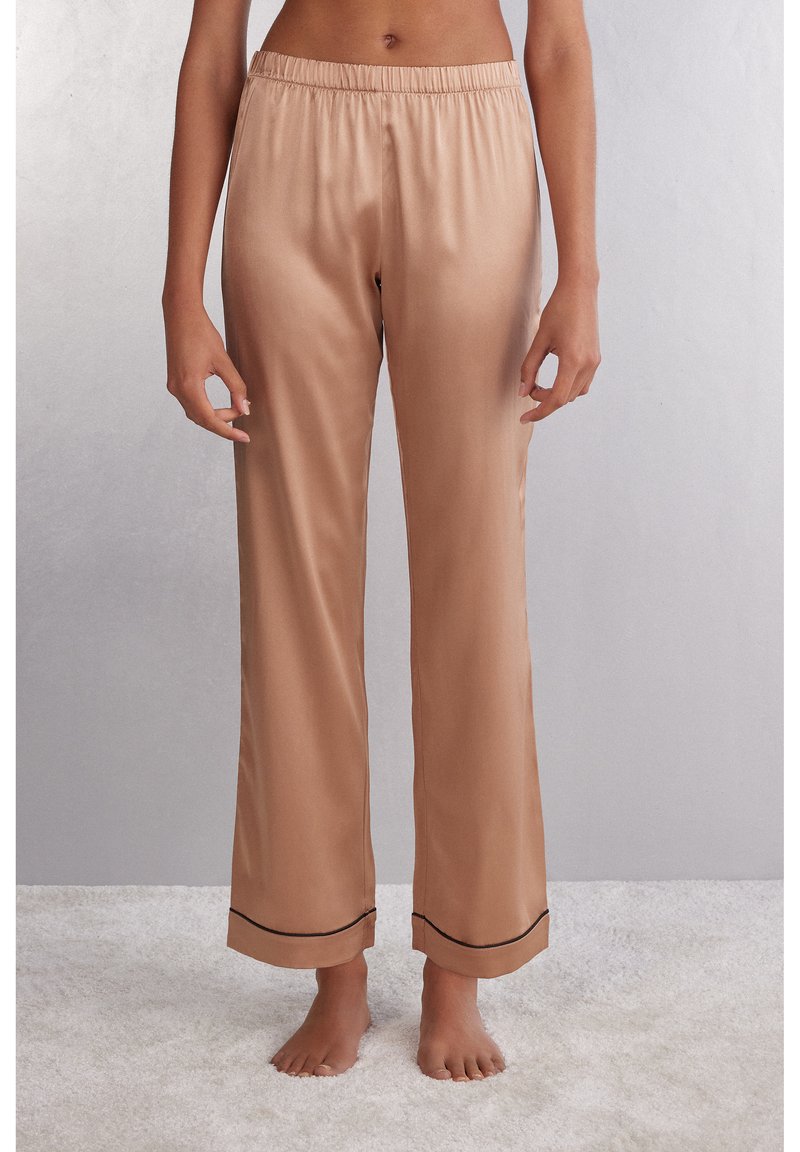 Satin pyjamabroek in lichtbeige met een elastische tailleband, rechte pijpen en zwarte bies langs de zoom. Soepele textuur.
