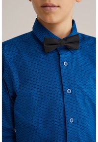 Blå skjorta med ett litet flugmönster, svart fluga och ljusblå knappar. Bomullsmaterial med en mjuk struktur.