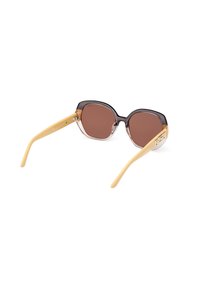 Gafas de sol con tintes marrones, marco transparente en tonos marrón y crema, con un diseño hexagonal y patillas amarillas con detalles metálicos.
