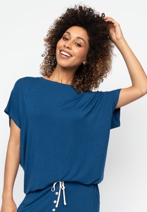 Top blu, a maniche corte, di taglio comodo, realizzato in tessuto morbido, con scollatura a girocollo e dettaglio con cordoncino all'orlo.